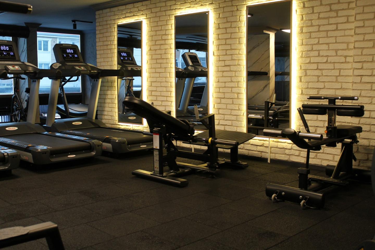 Space Gym: tuğla duvar önünde koşu bantları, aydınlatmalı aynalar ve ağırlık sehpaları